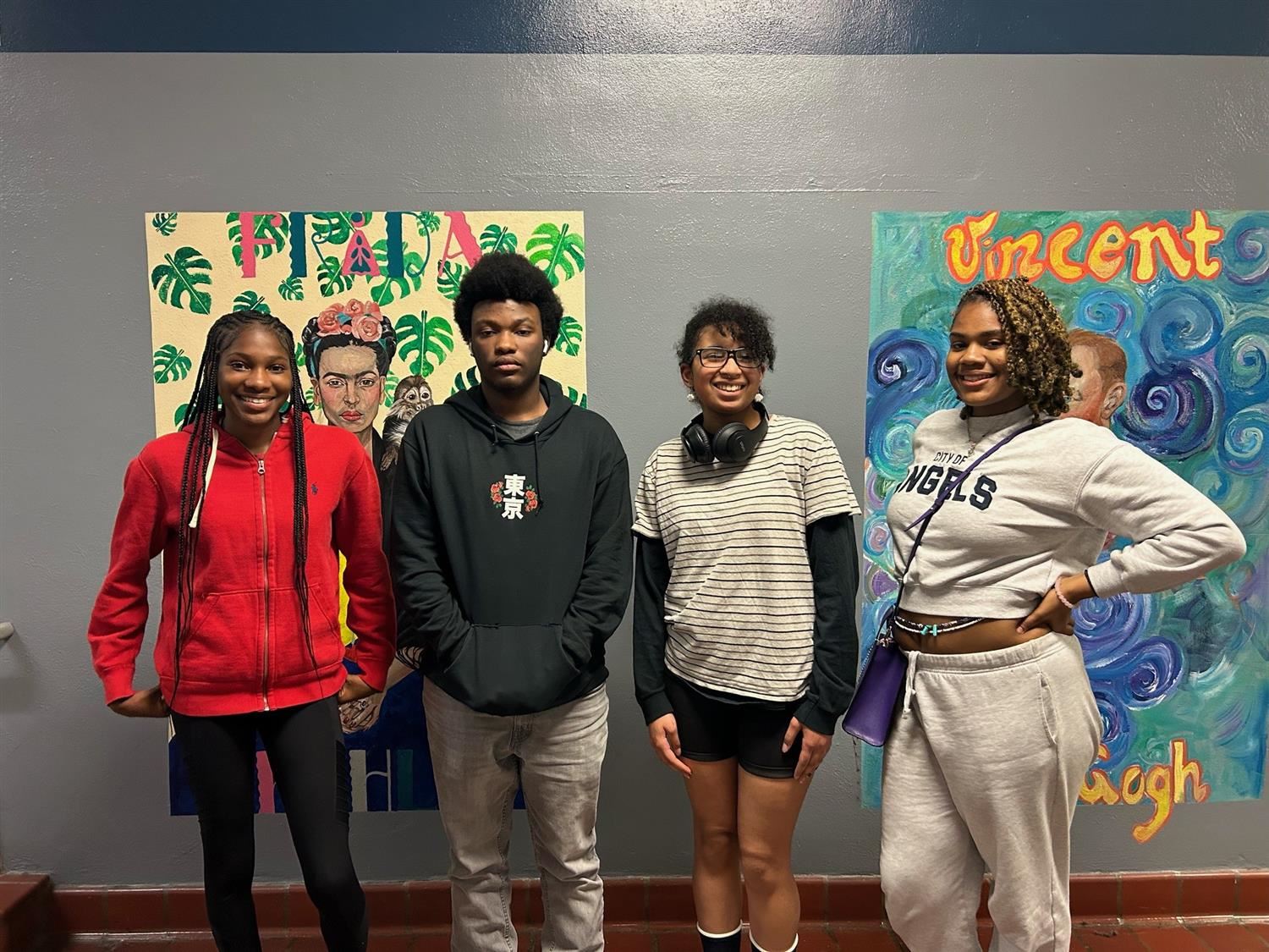 four students standing shoulder to shoulder in front of patterned artwork